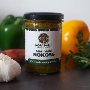 Marinade base aromatique Nokoss Moss Dolli dans un pot en verre, posée à côté d’ingrédients frais comme ail, oignon, persil et poivron