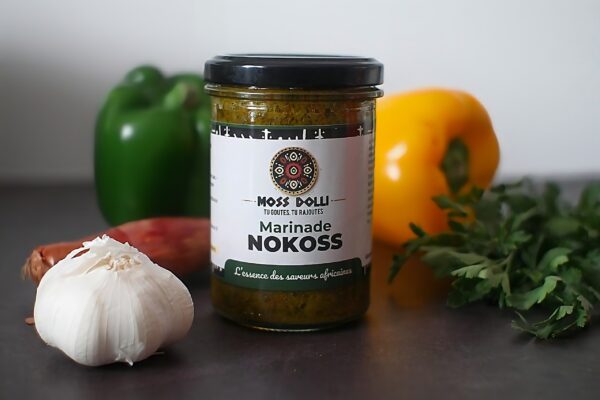 Marinade base aromatique Nokoss Moss Dolli dans un pot en verre, posée à côté d’ingrédients frais comme ail, oignon, persil et poivron
